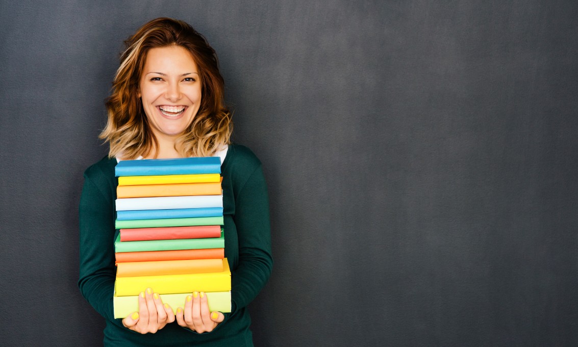 Smilende kvinne som bærer en stor bunke bøker