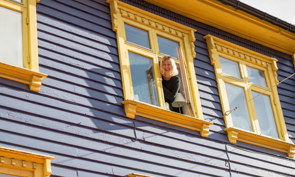 Ung kvinne titter ut av et vindu i et fargerikt trehus