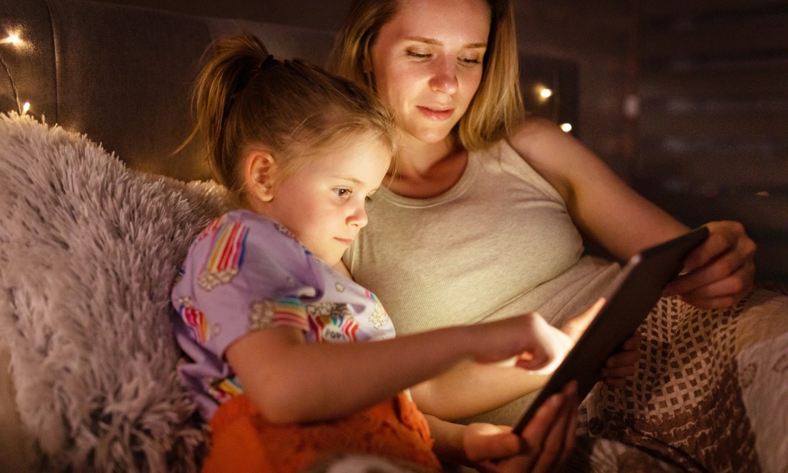 liten jente og kvinne sitter i sofa og ser på ipad sammen