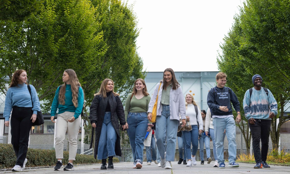 10 studenter gående ute på campus i fint vær.