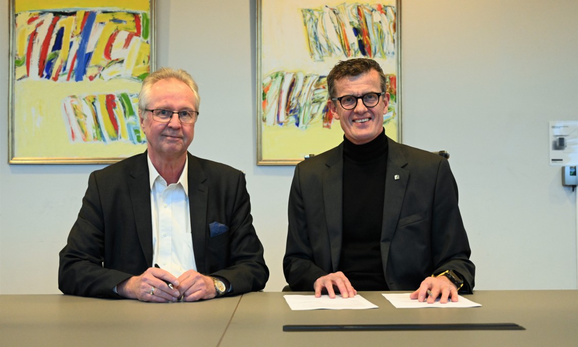 To dresskledde menn signerer en avtale i et møterom