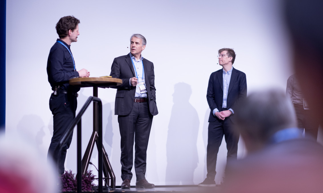En konferansier stiller spørsmål til to foredragsholdere.