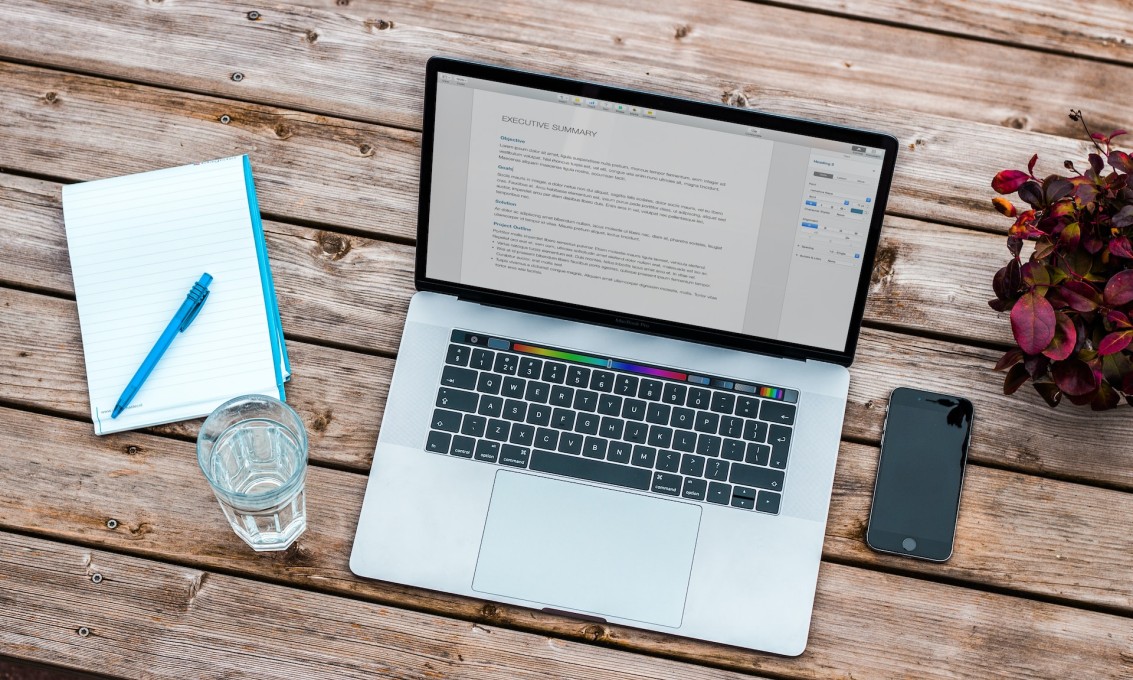 Illustrasjonsfoto av en åpen laptop, telefon, notatblokk og et glass vann.