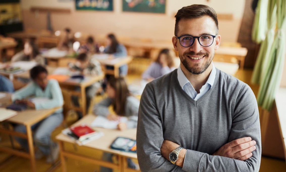 mann smiler til kamera, står foran elever i et klasserom