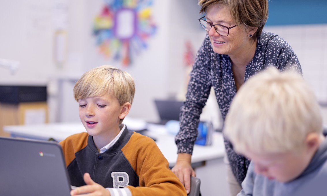 Lærer hjelper elev med oppgave på PC i et klasserom. 