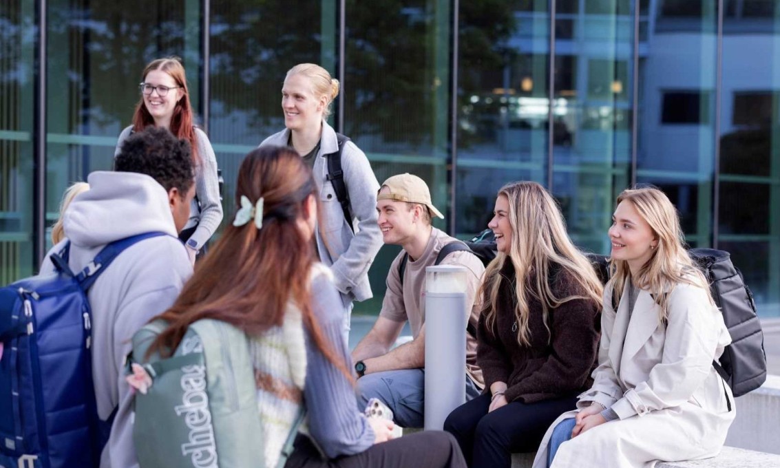 Studenter sitter på benker utenfor bygg med glassvegger på campus.