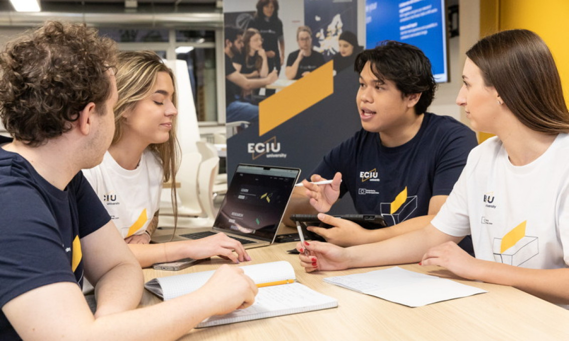 Four students sitting around a table with a rollup that says "ECIU" behind them.