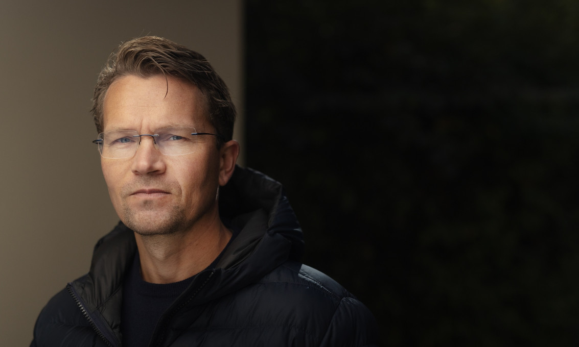 Mann ser inn i kamera. Mørk bakgrunn.