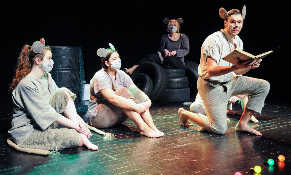 Fire dramastudenter fremfører på en scene i kostymer.