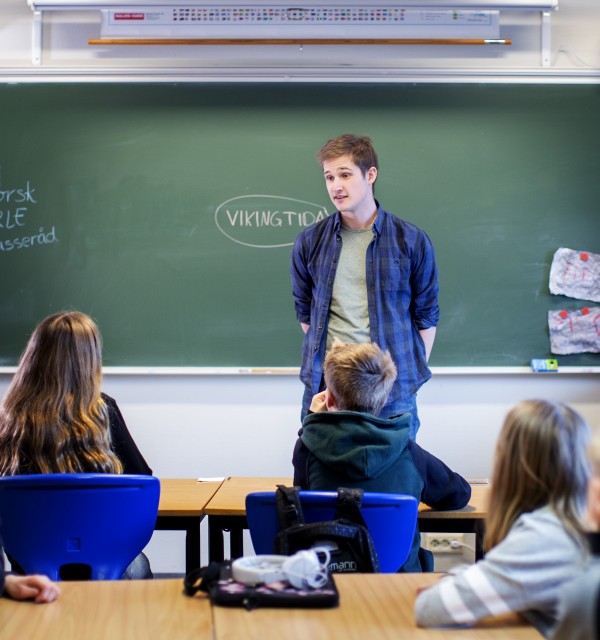 Mannlig lærerstudent står foran tavle og elever i klasserom