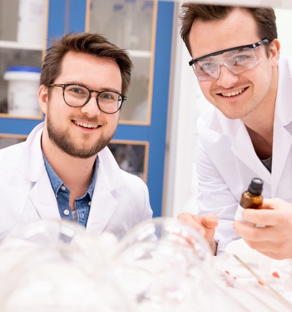 To mannlige studenter i labfrakk jobber på et laboratorium