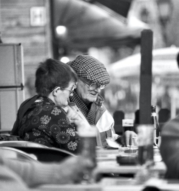 En eldre mann og dame leser avis på kafe.