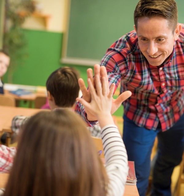 Mannlig lærer gir "high five" til en ung barneskoleelev i et klasserom