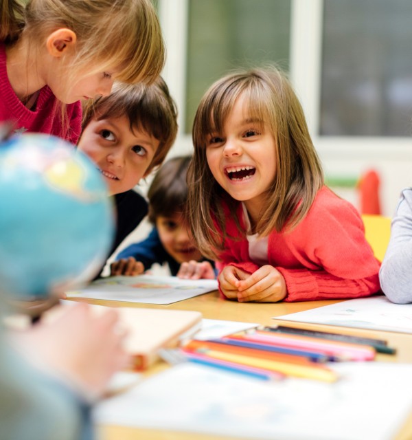 Barn smiler og ler rundt et bord i et klasserom