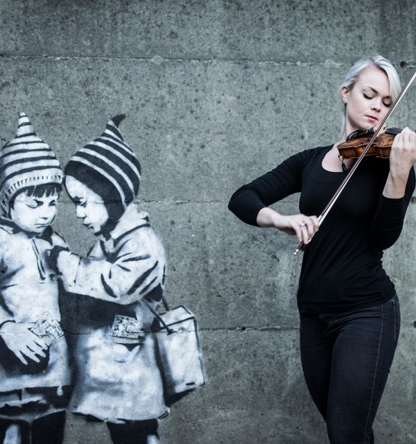 Kvinnelig fiolinist spiller i Stavanger sentrum foran grafitti
