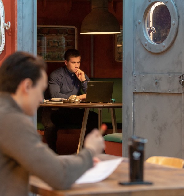 En student studerer ved et bord, mens en annen student studerer i en av tankene i Dataverkstedet