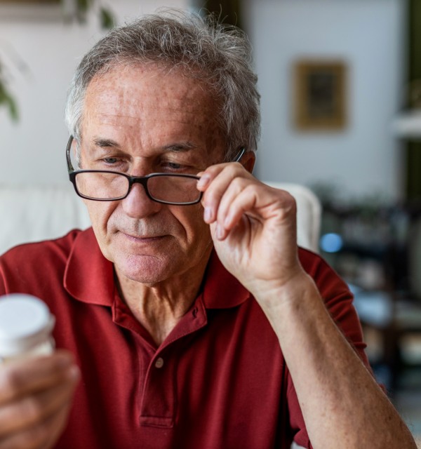 En eldre mann med briller studerer en pilleboks