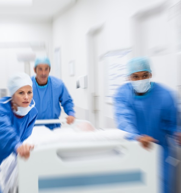 Tre helsepersonell i blå uniform transporter pasientseng til operasjonsstuen