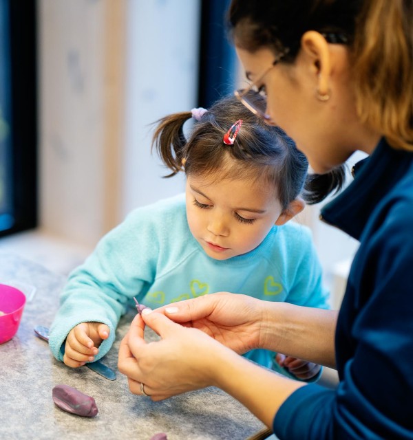 Kvinnelig barnehageansatt hjelper liten jente i barnehage med et kunst- og håndverksprosjekt