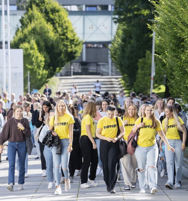 En stor gruppe studenter, flere med gule Fadder-t-skjorter, går på campus