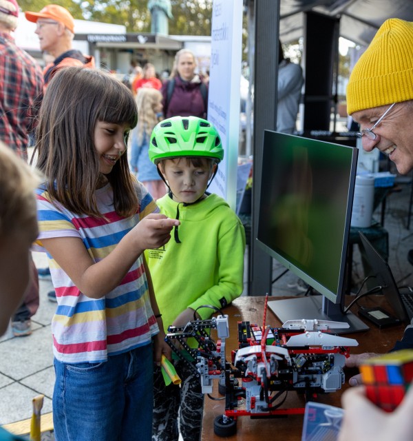 Jente og gutt ser på legorobot sammen med smilende mann