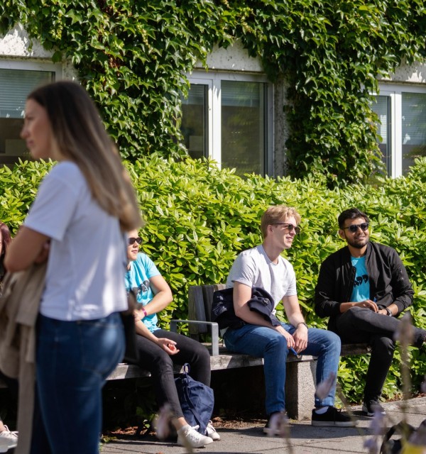 Studenter sitter på benker foran bygning med eføy på veggen