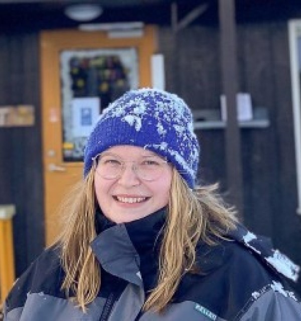 ung kvinne med termodress og fiolett vinterlue smiler til kamera. Det er snø på lua hennes.
