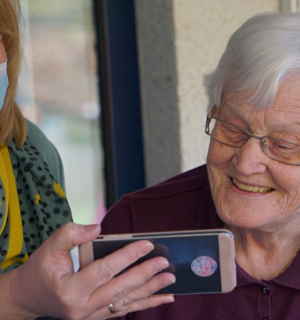 eldre dame ser på en mobil holdt av en annen yngre person