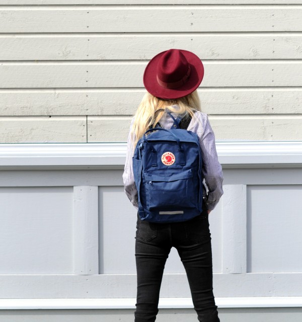 Jente med blå sekk og rød hatt ser inn i en vegg.