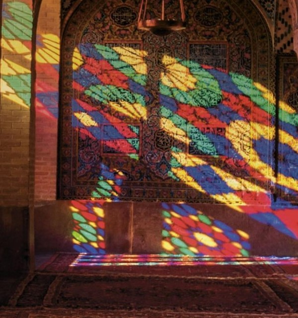 interiør fra moské, sollys gjennom fargede glass lyser opp et mørkt rom i mange farger