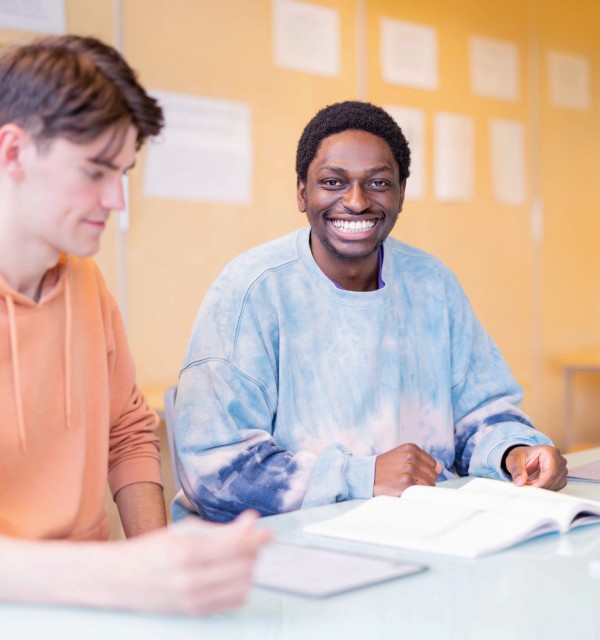 To studenter i et klasserom med hver sin skrivebok foran seg.