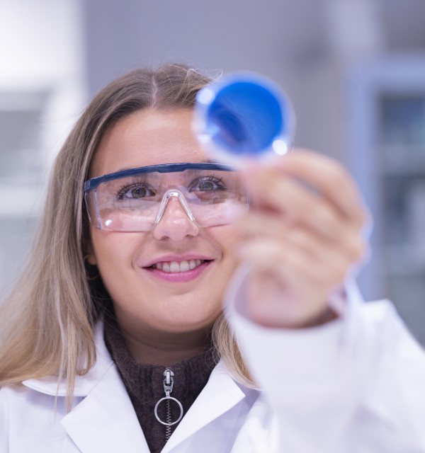 En student ser på en beholder med blå væske. Hun er på et laboratorium. Foto.