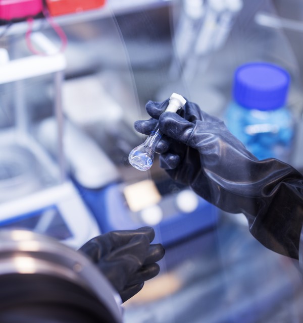 En person med svart hanske jobber inni en maskin på et laboratorium. 