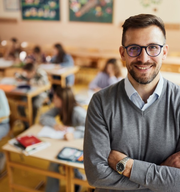 mann smiler til kamera, står foran elever i et klasserom