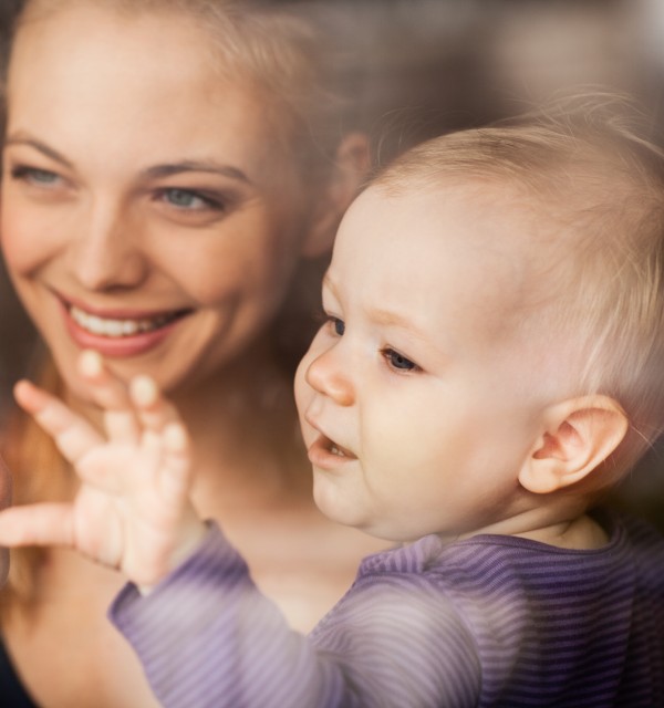 En kvinne holder et lite barn og peker ut gjennom et vindu