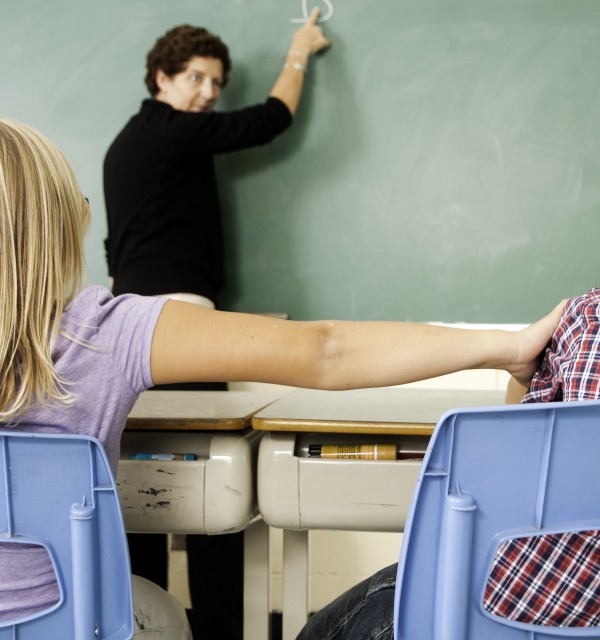 Klasseromssituasjon der en elev dytter en annen. Læreren snur seg fra tavla og ser hva som skjer. Foto: iStock.