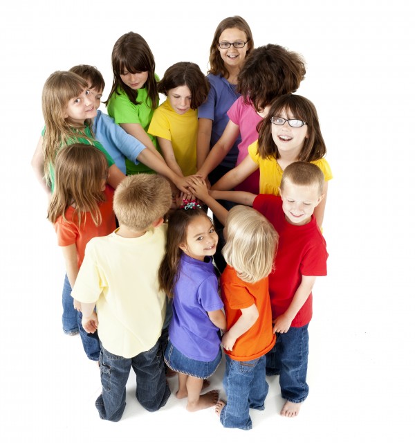En gruppe barn i forskjellig alder står i en sirkel med en hånd hver inn mot midten. Foto: iStock.