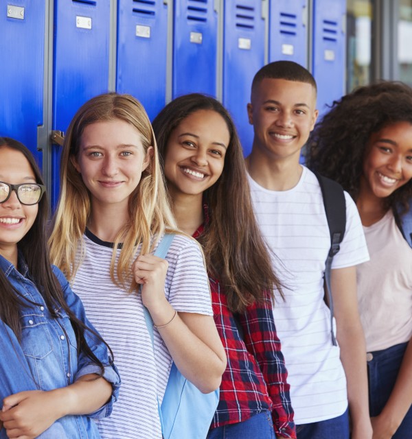 En gruppe smilende ungdommer står etter hverandre ved en skaprekke på en skole.