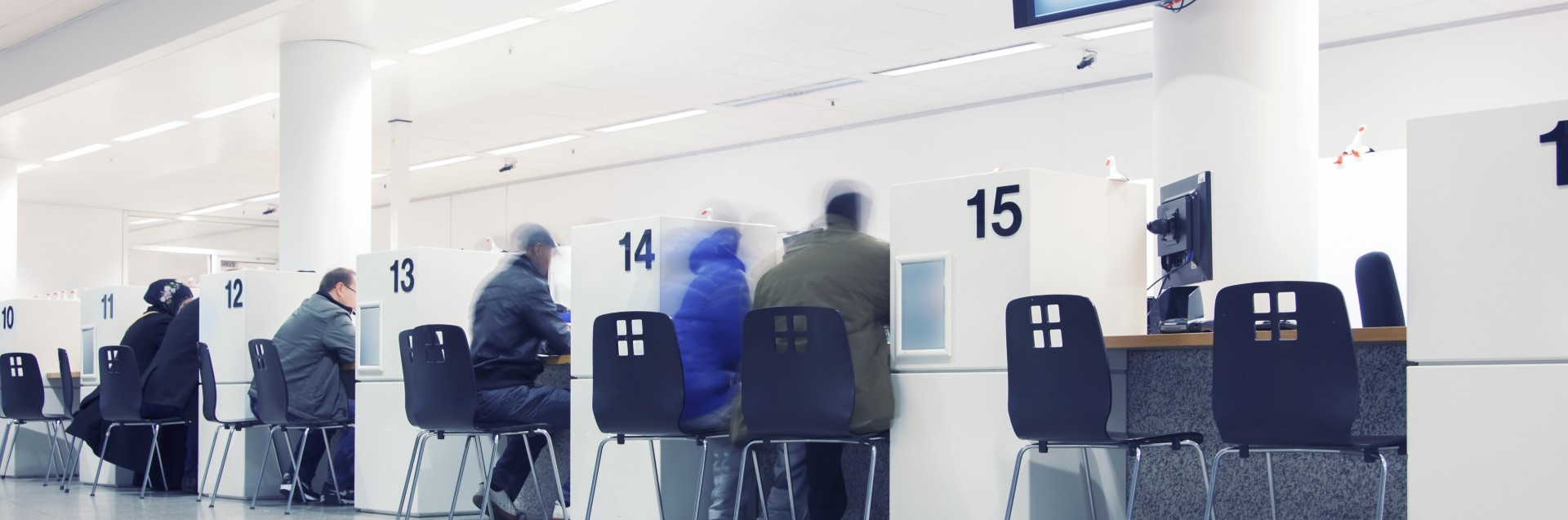 Personer med ryggen til sittende foran skranke på offentlig kontor