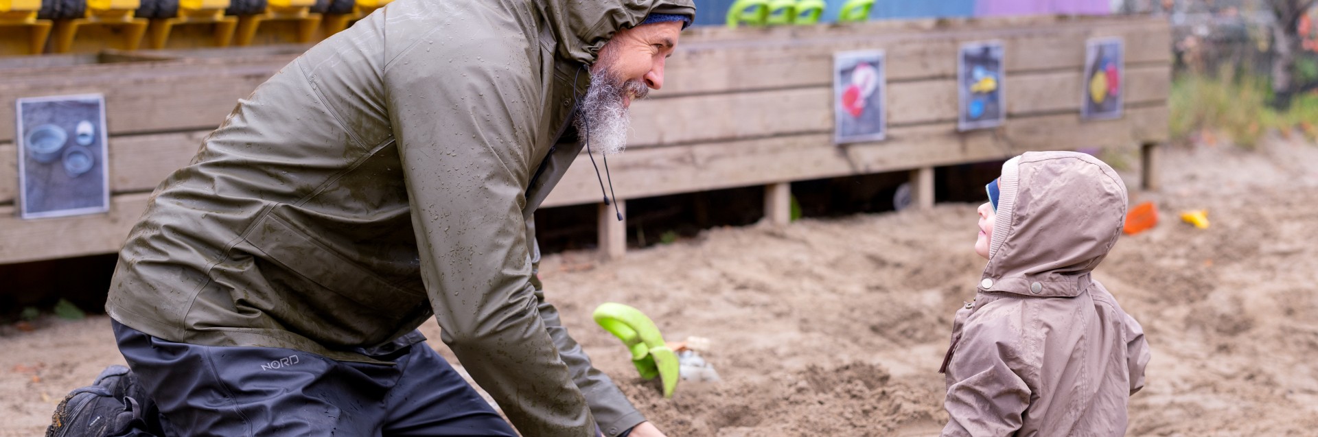 En voksen og et barn leker i sandkassen på en regnfull dag. Foto: Elisabeth Tønnessen/Læringsmiljøsenteret, UiS