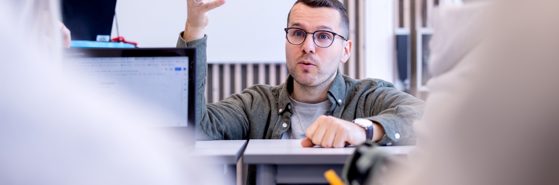 En mann sitter på huk ved en pult i et klasserom. Foto: Elisabeth Tønnessen/ Læringsmiljøsenteret, UiS
