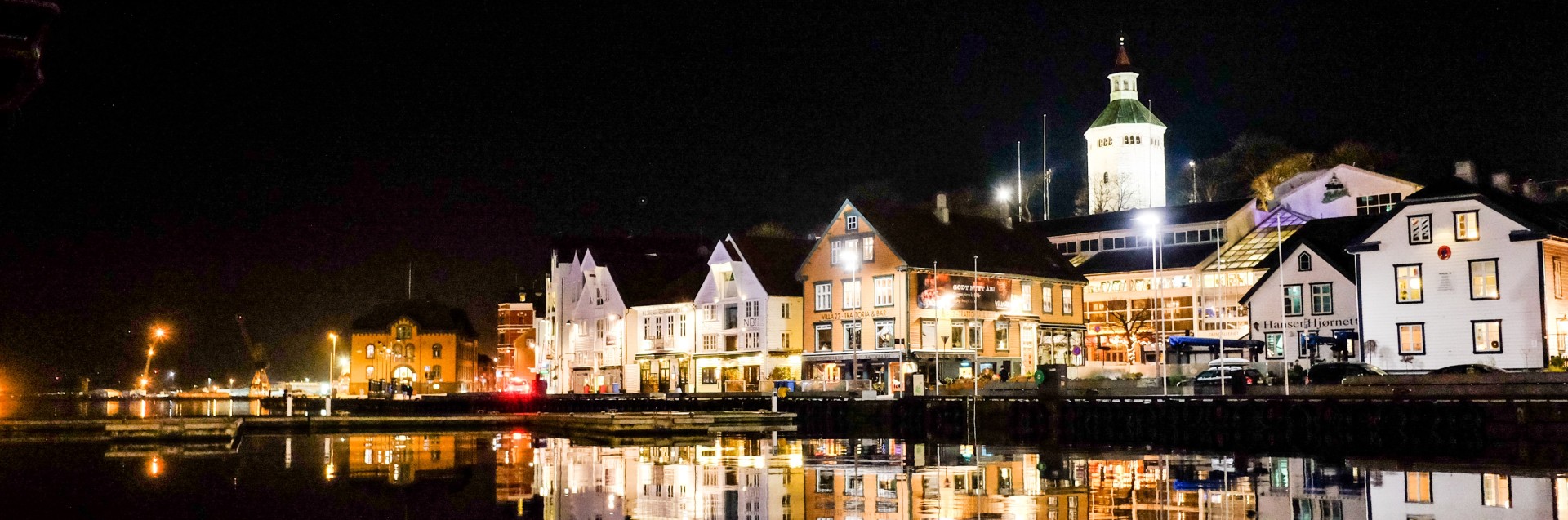 Bilde om natten av bygninger langs havnen i en by.