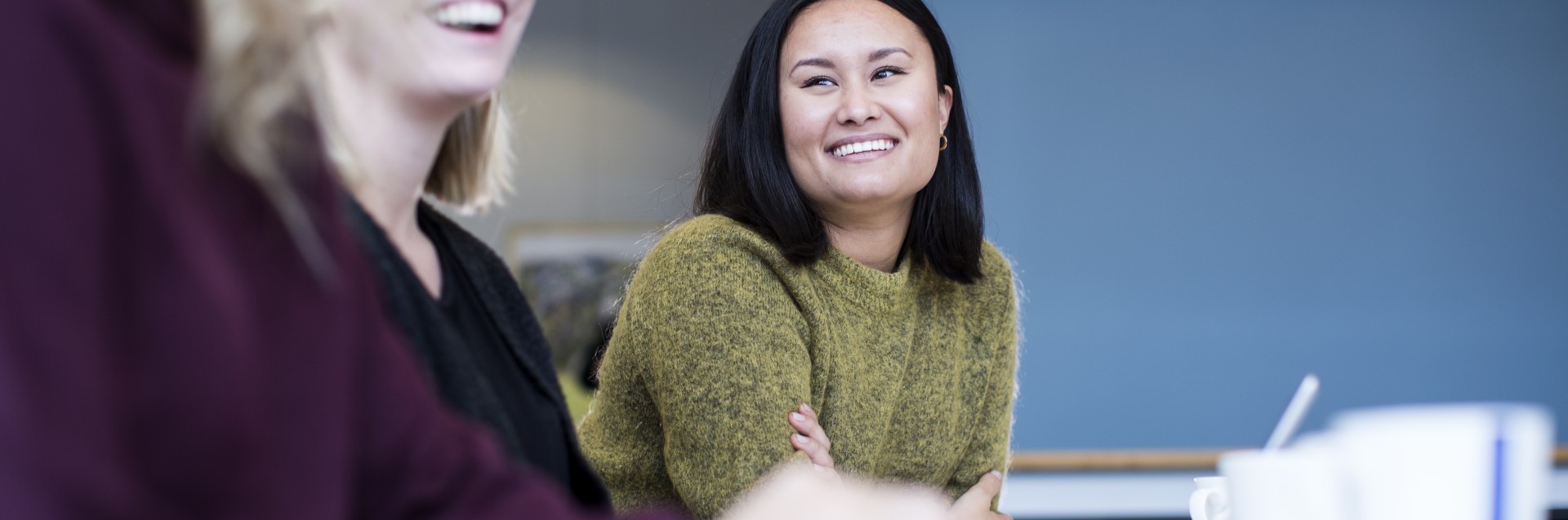 Tre kvinnelige studenter sitter på rekke og ser smilende på hverandre.
