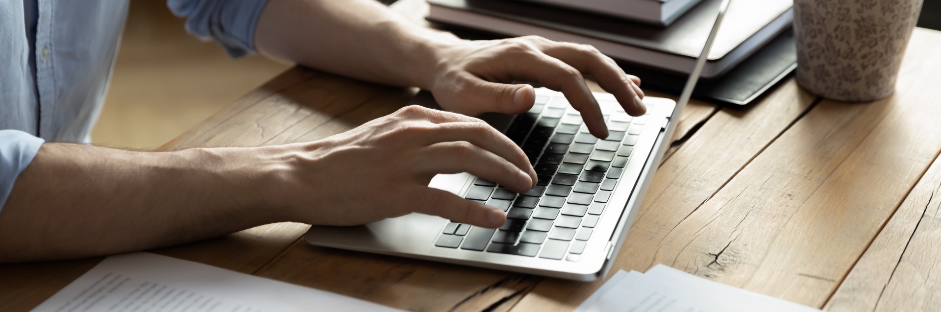 Mann som skriver på bærbar pc omgitt av bøker og sakspapirer. Foto: Getty Images.