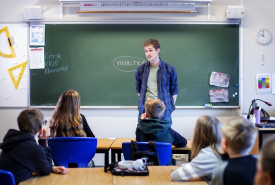Mannlig lærerstudent står foran tavle og elever i klasserom