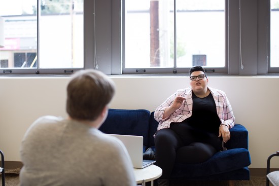Bildet viser en to personer som snakker sammen. Den ene sitter med ryggen til.
