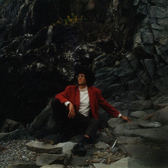 Artisten Beharie sitter i et stenbrudd med rød jakke.
