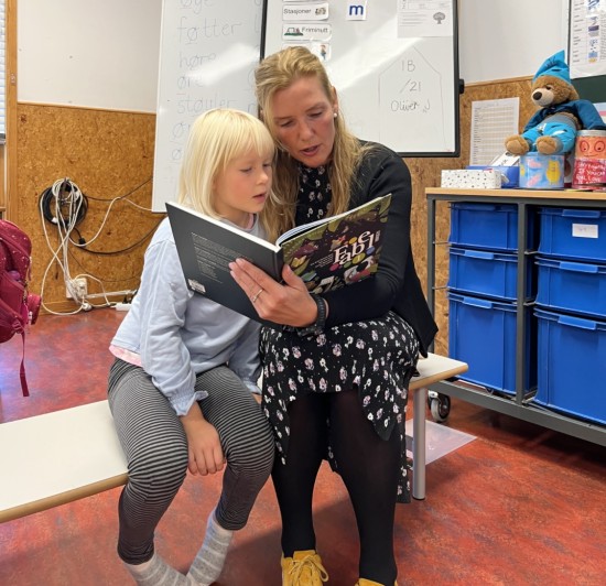 6 år gammel jente og kvinnelig lærer leser boken FABEL på en benk i klasserommet.