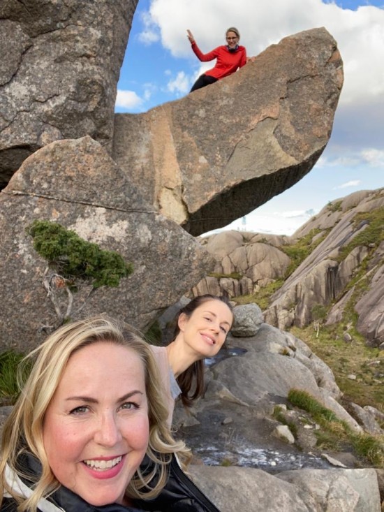 Selfie av tre kvinner ute i naturen. To av dem står foran en steinformasjon, mens den tredje kvinnen ligger oppå steinen i bakgrunnen.