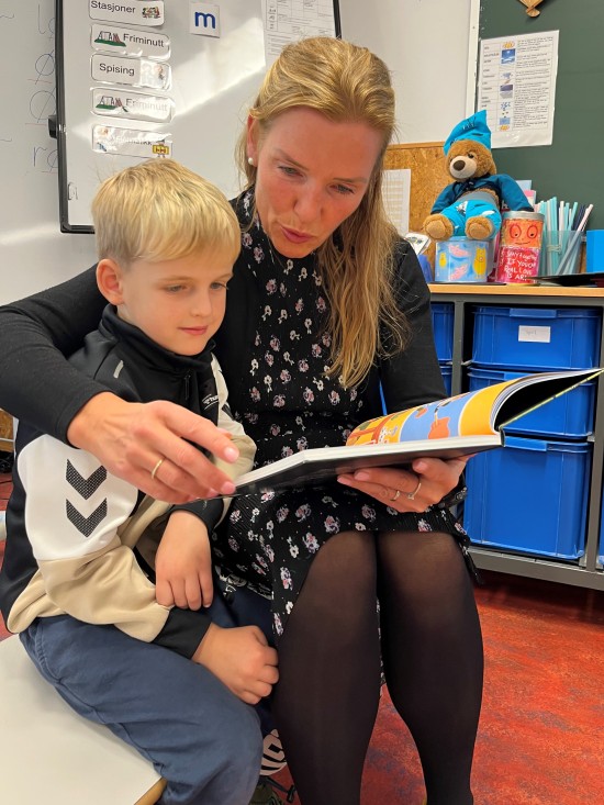 Gutt 6 år og voksen kvinne leser en bok sammen i et klasserom
